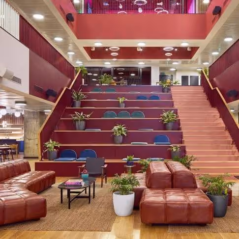 Modern workspace with tiered seating, potted plants, leather couches, and stairs.